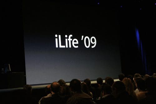 A large screen displays the text 'iLife '09' during a presentation, with an audience visible in the foreground attentively watching the event.