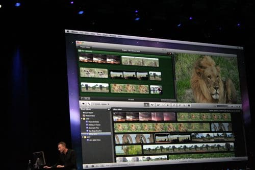A presentation scene featuring a man seated at a desk, focusing on a computer screen displaying video editing software with various clips of nature and a prominent close-up of a lion.