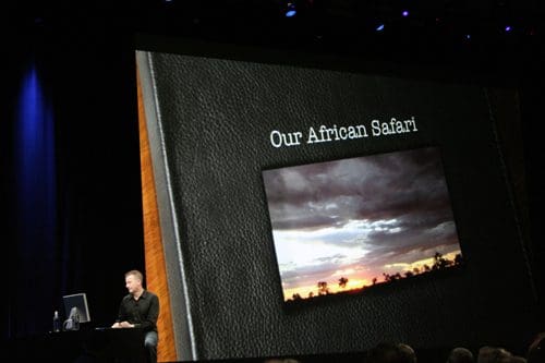 A speaker at a conference presenting a slideshow titled 'Our African Safari,' featuring a scenic photograph of a sunset over an open landscape, displayed on a large screen behind him.