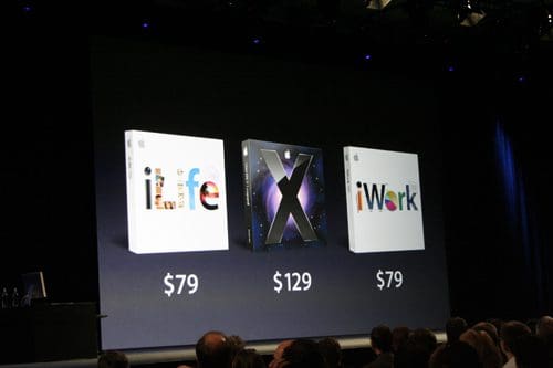 Three software boxes displayed on a large screen during a presentation, labeled 'iLife' for $79, 'X' for $129, and 'iWork' for $79. The background is dark with an audience in the foreground.