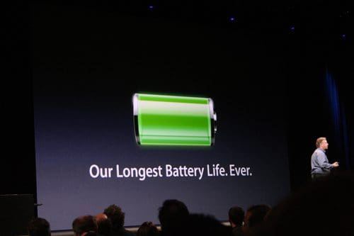 A speaker on stage points to a large screen displaying a green battery icon, indicating full charge, alongside the text 'Our Longest Battery Life. Ever.' The audience is partially visible in the foreground.