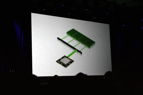 A large presentation screen displays a diagram illustrating a computer chip connected to a memory module with green connectors. The audience's silhouettes are visible in the foreground.