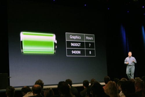 A presenter speaks to an audience, with a large display showing a battery icon that is almost fully charged. Next to it, a table lists two graphics models, 9600GT with 7 hours and 9400M with 8 hours of usage.