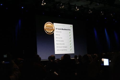 A presentation at a tech event showcasing a large screen with a checklist for the 17-inch MacBook Pro, highlighting features like mercury free and 2009 EPA Gold Certification, with an audience in the foreground.