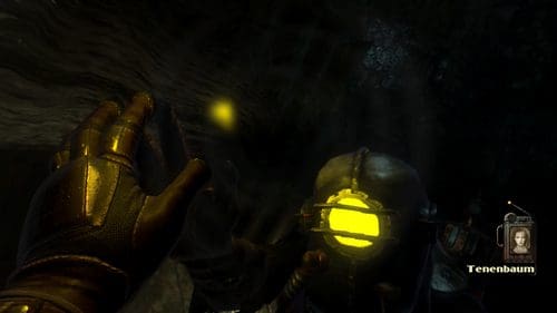 A close-up view of a diver in dark underwater surroundings, wearing a helmet with a bright yellow light. The diver's gloved hand reaches out towards a small glowing object, surrounded by swirling water.