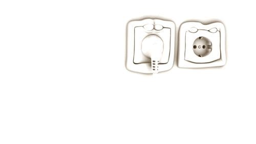 A close-up view of a white electrical outlet featuring two distinct sockets. The left socket is designed for a specific plug type, while the right socket has a round shape with multiple holes.