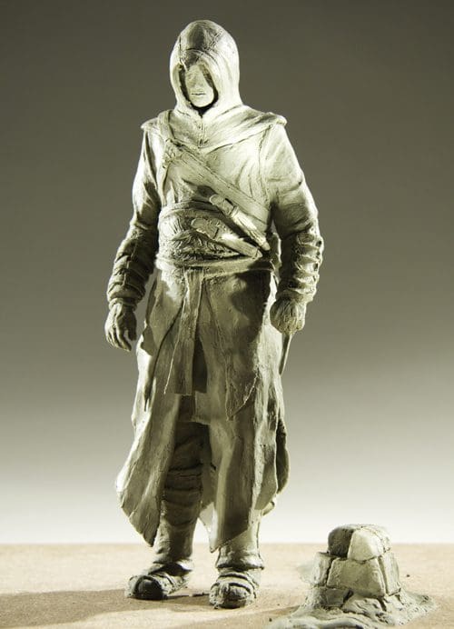 A detailed sculpture of a hooded figure standing in a contemplative pose, dressed in a flowing robe with various adornments. The figure's face is obscured by the hood, adding an air of mystery. A small stone pedestal is positioned next to the figure.