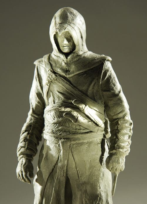A detailed sculpture of a hooded figure dressed in a flowing garment, holding a hidden blade and standing in a confident pose against a neutral background.