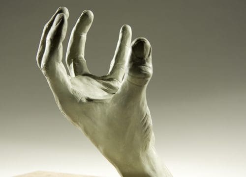 A sculpted hand with fingers slightly curled, reaching outward against a neutral background. The texture of the sculpture highlights the details of the skin and fingernails, creating a lifelike appearance.