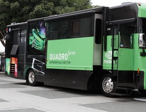 A green and black bus showcasing a Quadro Fermi advertisement, featuring the slogan 'Exponentially Better' on the side. The bus is parked on a plaza with trees in the background.