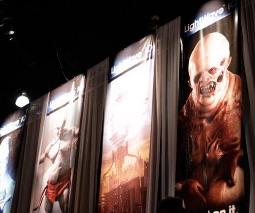 Vertical banners displayed at an event showcasing characters from a fantasy or science fiction theme. Each banner features detailed illustrations, with one showing a muscular figure and another depicting a grotesque creature in a dimly lit space.