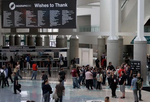 A crowd gathered in a spacious convention center, with individuals lining up near a registration desk. A large sign overhead displays the text 'Wishes to Thank,' while various attendees chat and interact in the modern environment.