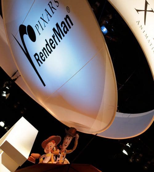 A large illuminated sign displaying 'PIXAR'S RenderMan' hangs above a stage, featuring animated characters Woody and Jessie from the Toy Story franchise peeking out from a red box.