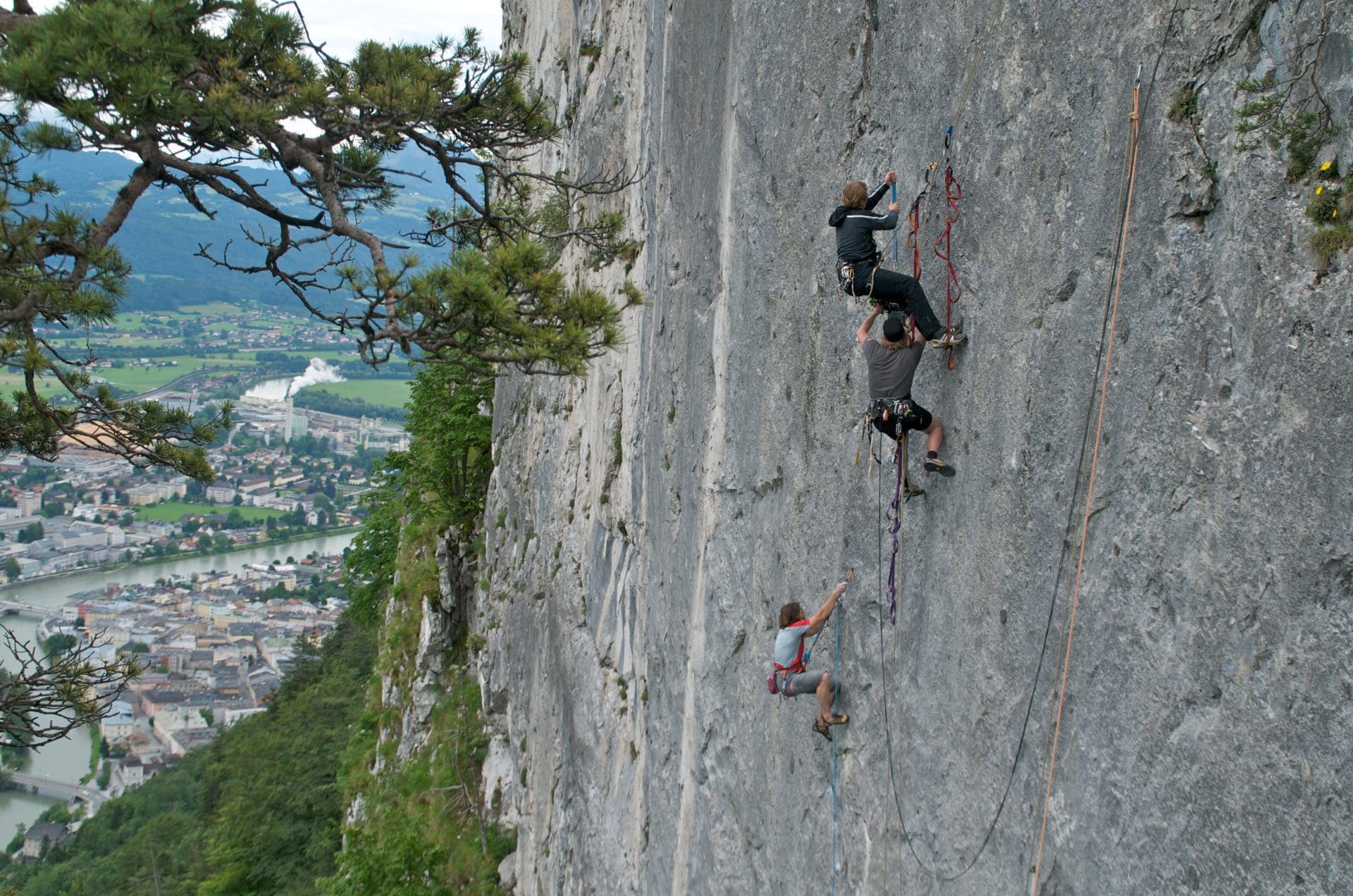 Three climbers scaling a steep rock face with a scenic valley below.