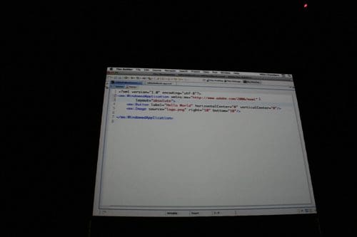 A computer screen displaying code in a text editor, showing HTML elements including a reference to Adobe's website and an image source. The background is dark, emphasizing the illuminated screen.