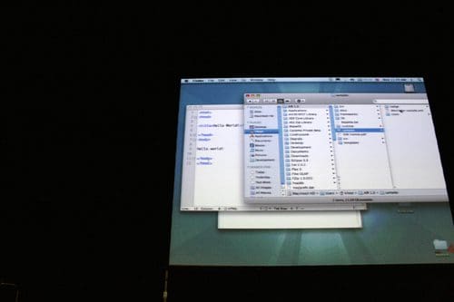 A projector screen displaying a computer desktop with a file directory open, showing various folders and documents on a teal background. The setting appears to be a presentation or workshop.