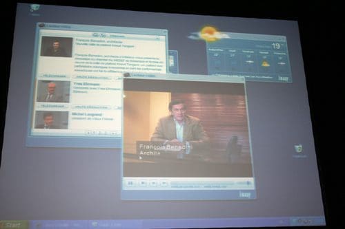 A computer screen displaying a video player featuring a speaker, alongside a news feed with multiple profiles on the left side. The weather widget in the top right corner shows a sunny forecast with a temperature of 19 degrees.