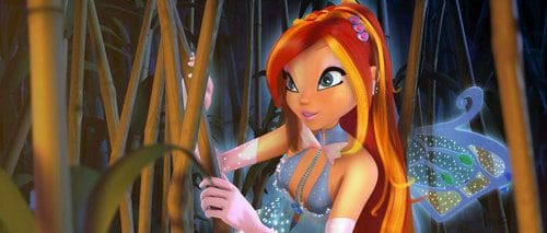 A fairy with vibrant red hair and large expressive eyes stands among tall green plants. She wears a delicate, shimmering outfit and looks intently at something in the foliage, with softly glowing wings behind her.