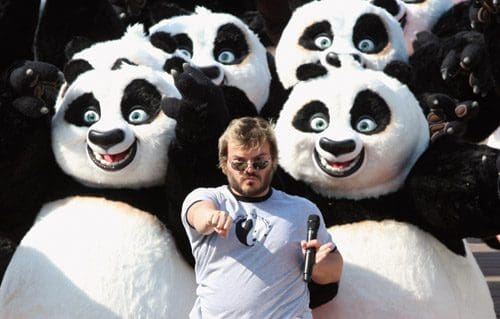 A man wearing sunglasses stands confidently with a microphone, surrounded by large, playful panda characters. The pandas have exaggerated expressions, creating a humorous and lively scene.
