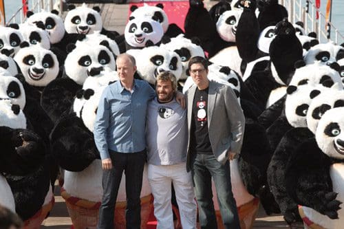 Three men posing happily in front of a large crowd of panda mascots on a wooden platform, with vibrant colors and a festive atmosphere.