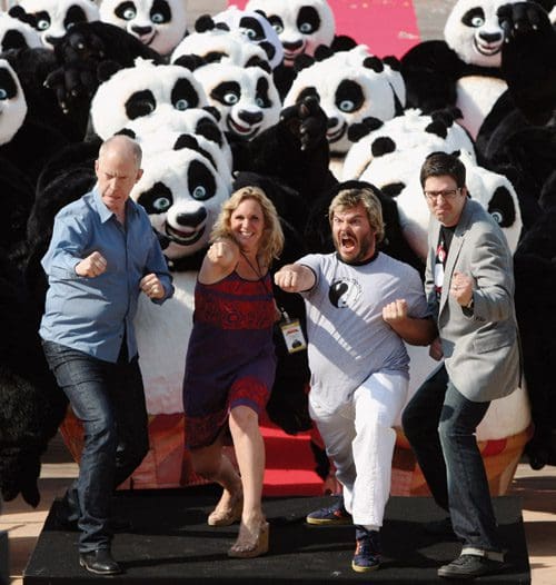 A group of four individuals, standing confidently and striking poses, in front of a crowd of panda mascots. The scene is lively, with vibrant colors and a festive atmosphere, showcasing the playful interaction between the people and the pandas.