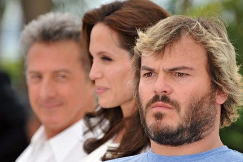 Three individuals posed for a photo outdoors: a man with gray hair and a white shirt smiling in the background, a woman with brown hair and a slight smile in the center, and a bearded man in a blue shirt looking serious in the foreground.