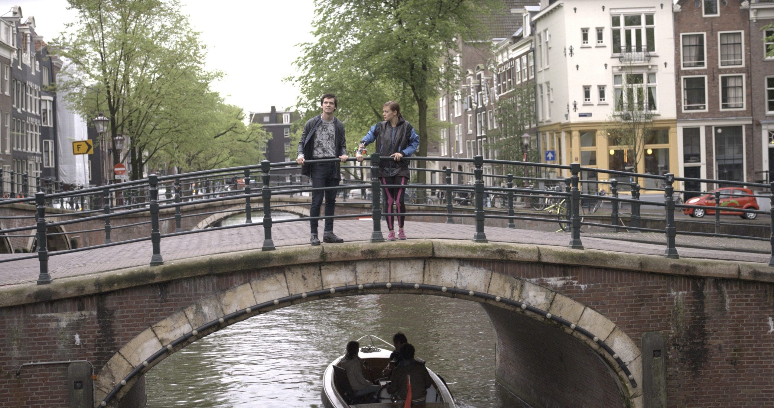 Two people standing on a canal bridge in Amsterdam with a boat below.