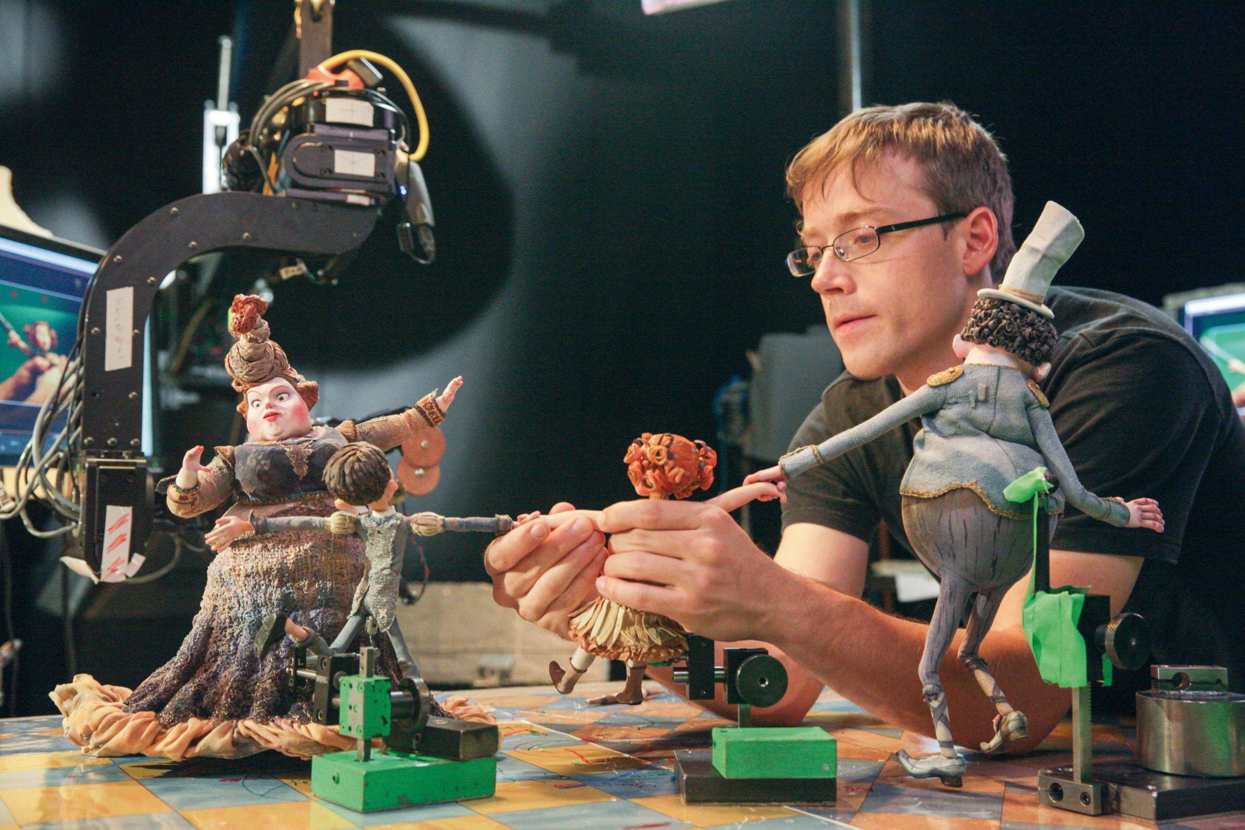 A puppeteer manipulating puppets on a set with cameras in the background.