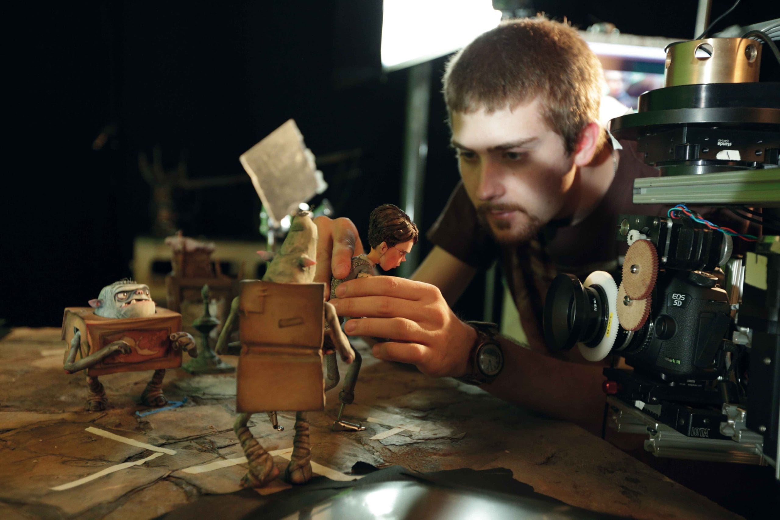 A person adjusting a stop-motion puppet next to a camera