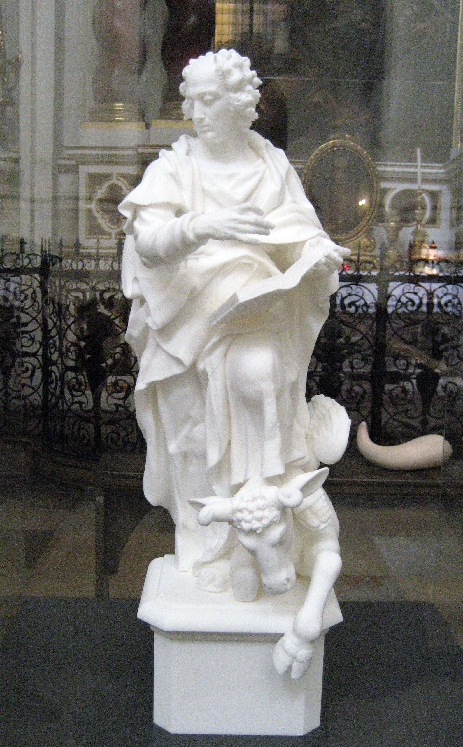 A white marble statue of a seated figure holding a book, with a calf at the base.
