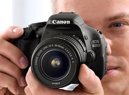 A person holding a Canon EOS 600D camera up to their face.