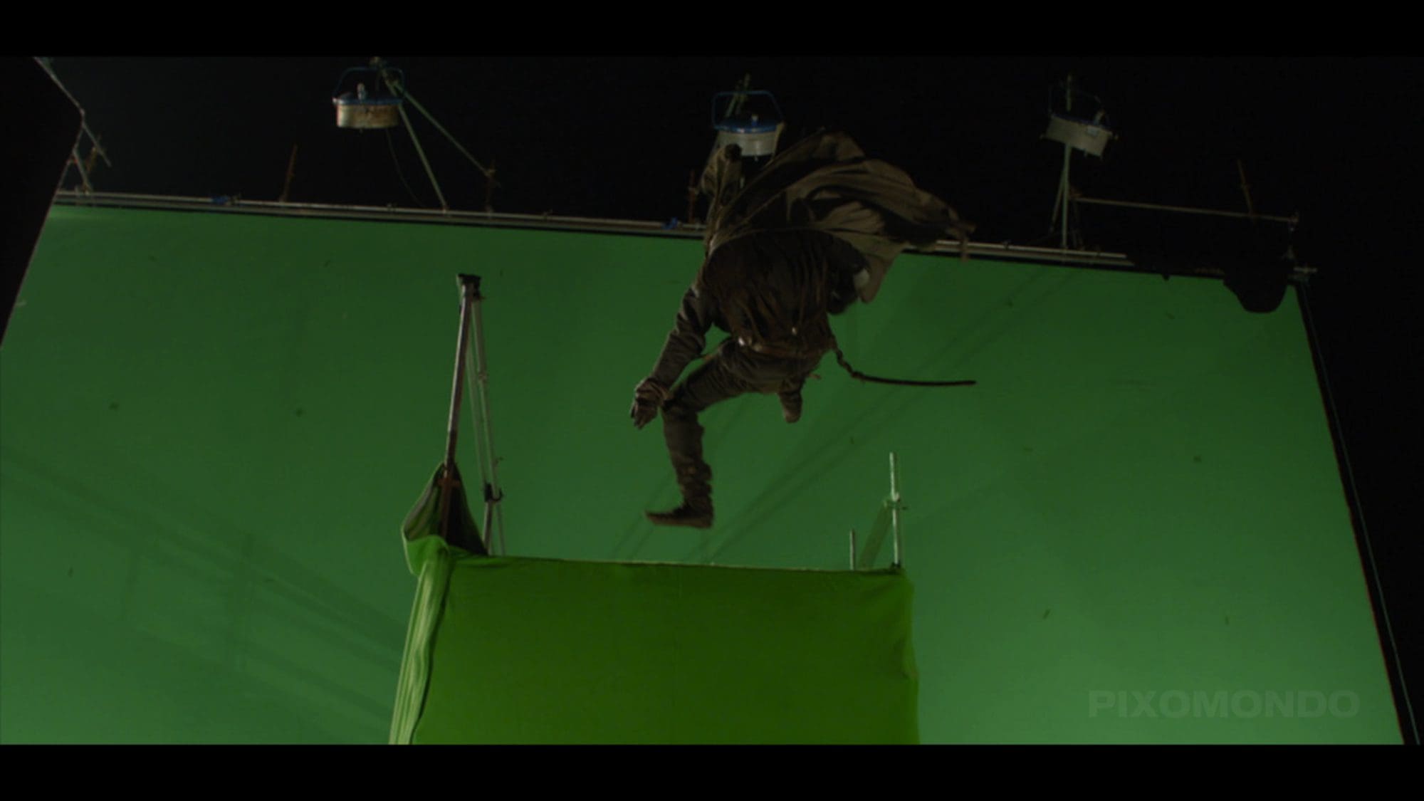 A stunt performer jumping over a green screen setup.