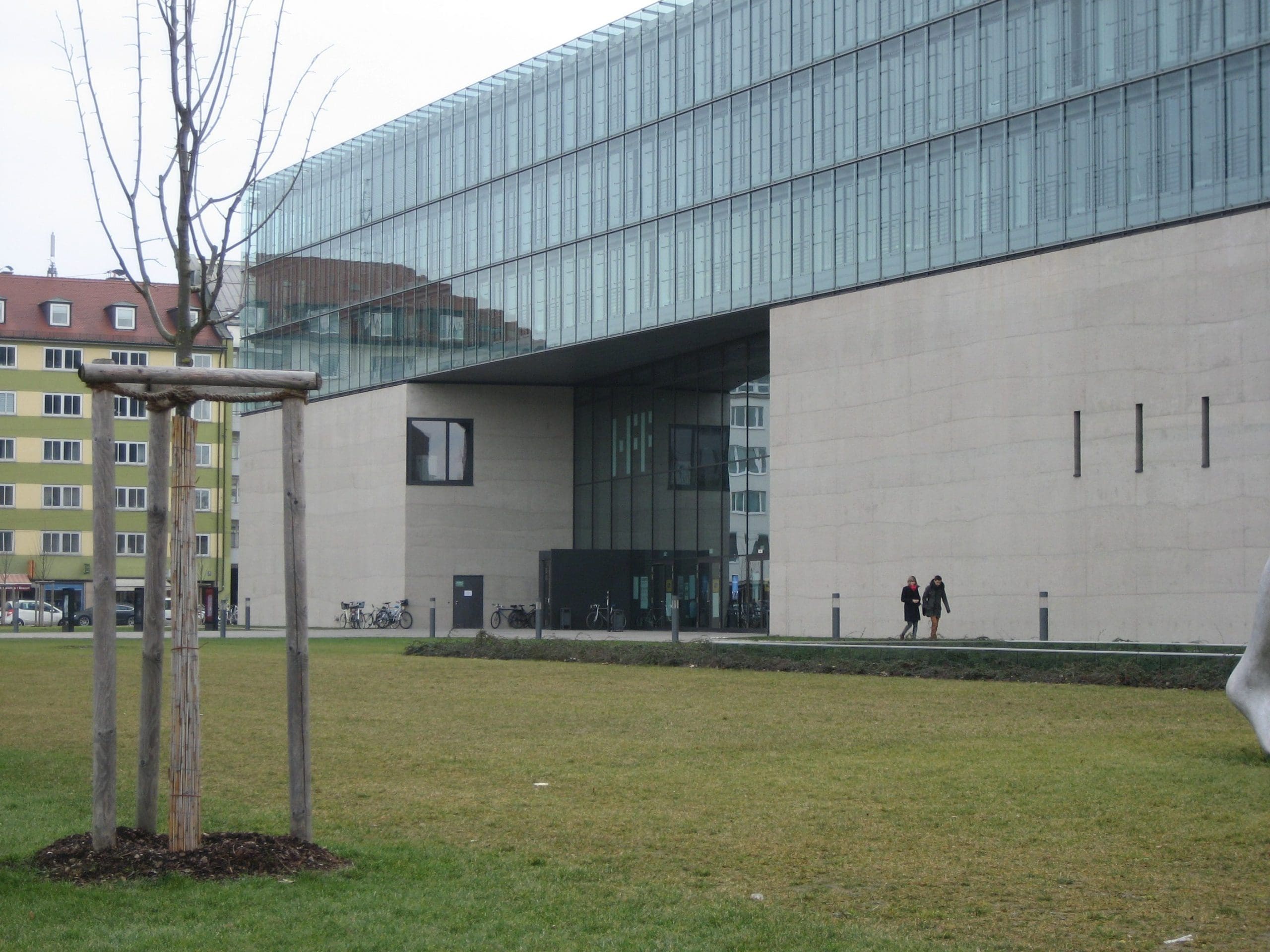 Modern glass building with grassy area and trees in foreground