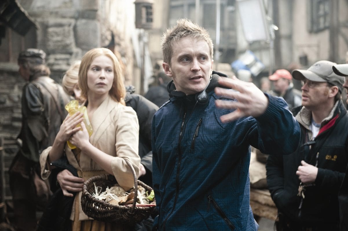 Director gesturing on film set with actors nearby.