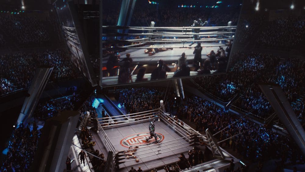 A large crowd watching a boxing match on a big screen in an arena.
