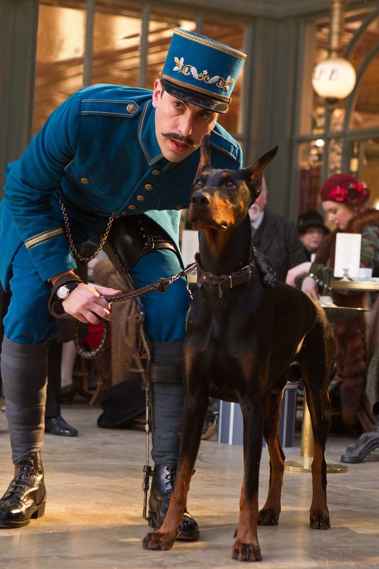 A man in a blue uniform with a dog in a lobby setting.