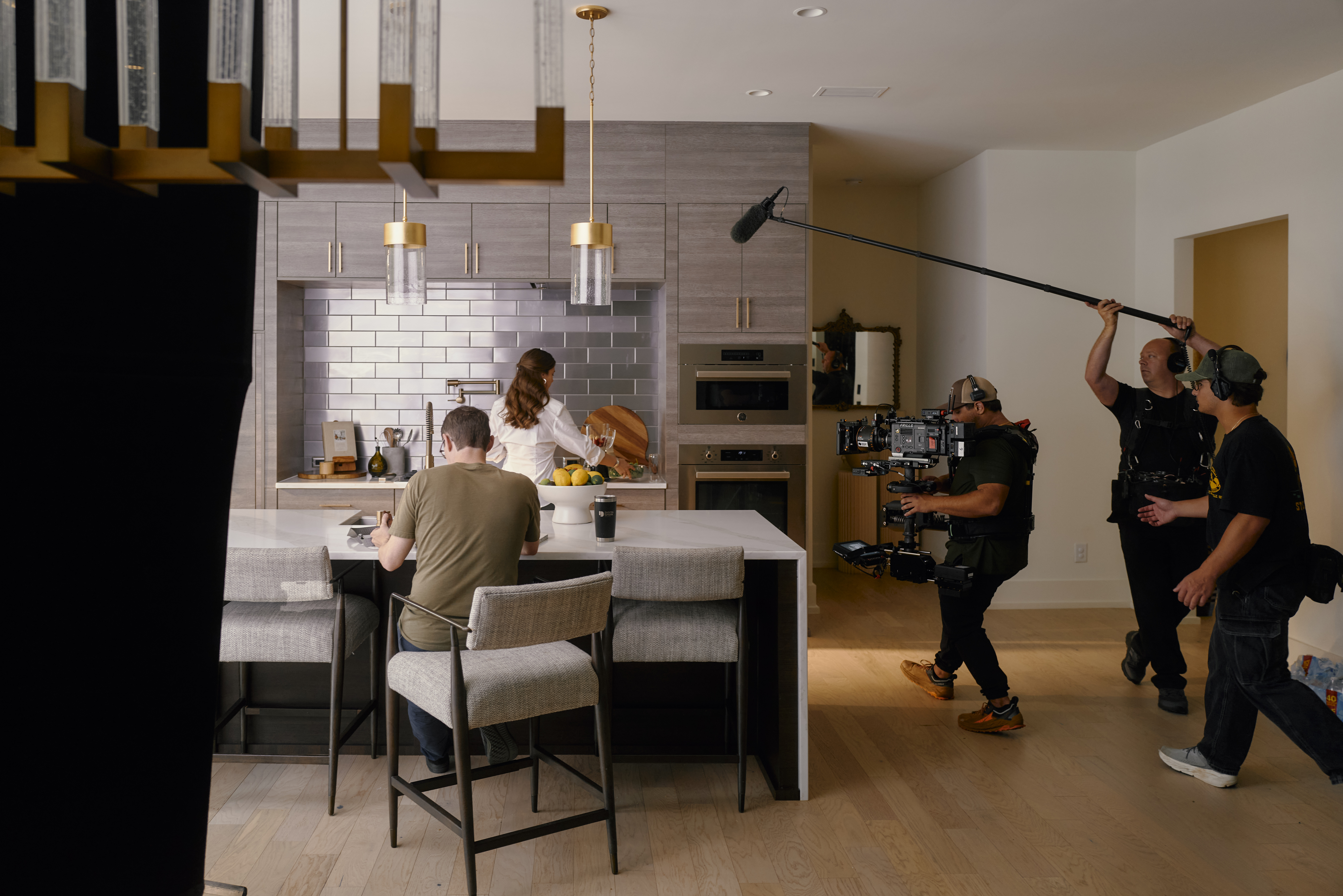 Commercial video production on set: a crew with a stabilized camera and a boom mic filming a couple in a kitchen