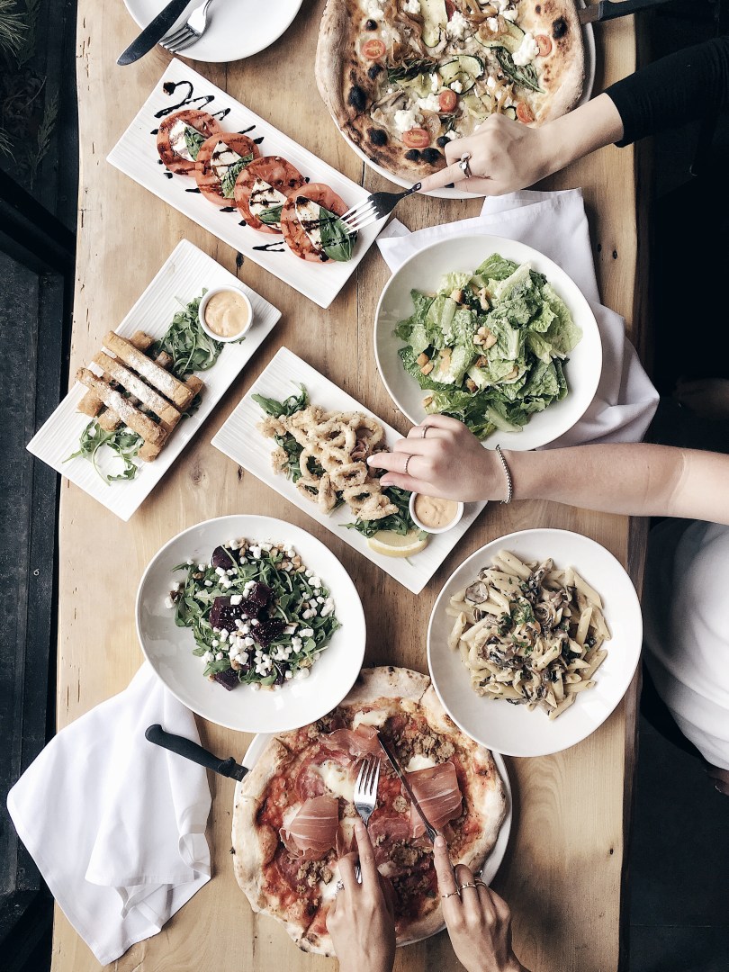 An aerial view of our feast at Lambretta Pizzeria, including calamari, caprese salad, vegetarian and meat pizzas, caesar salad and penne pasta