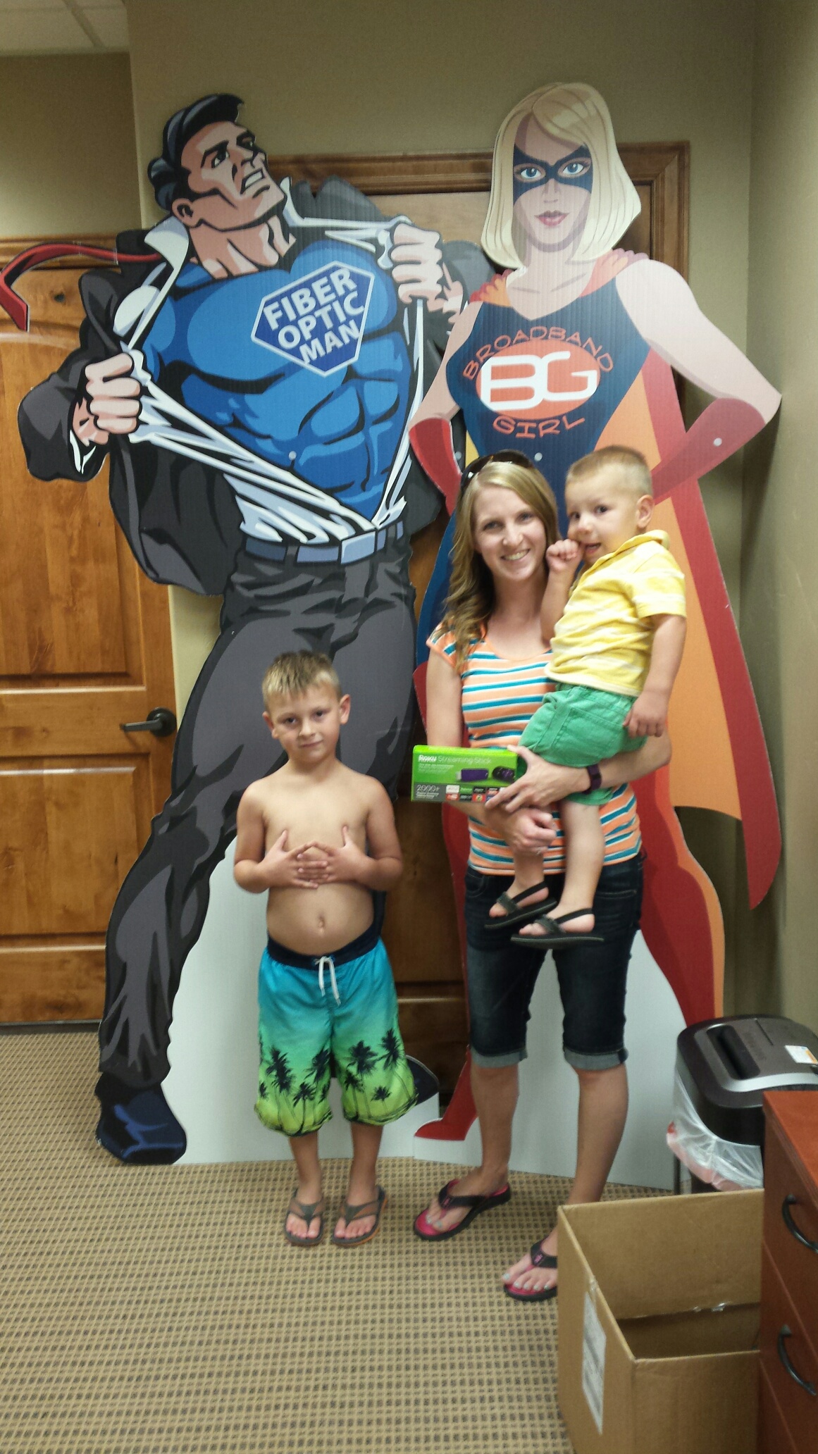 Family posing with a superhero cutout in a wooden room.