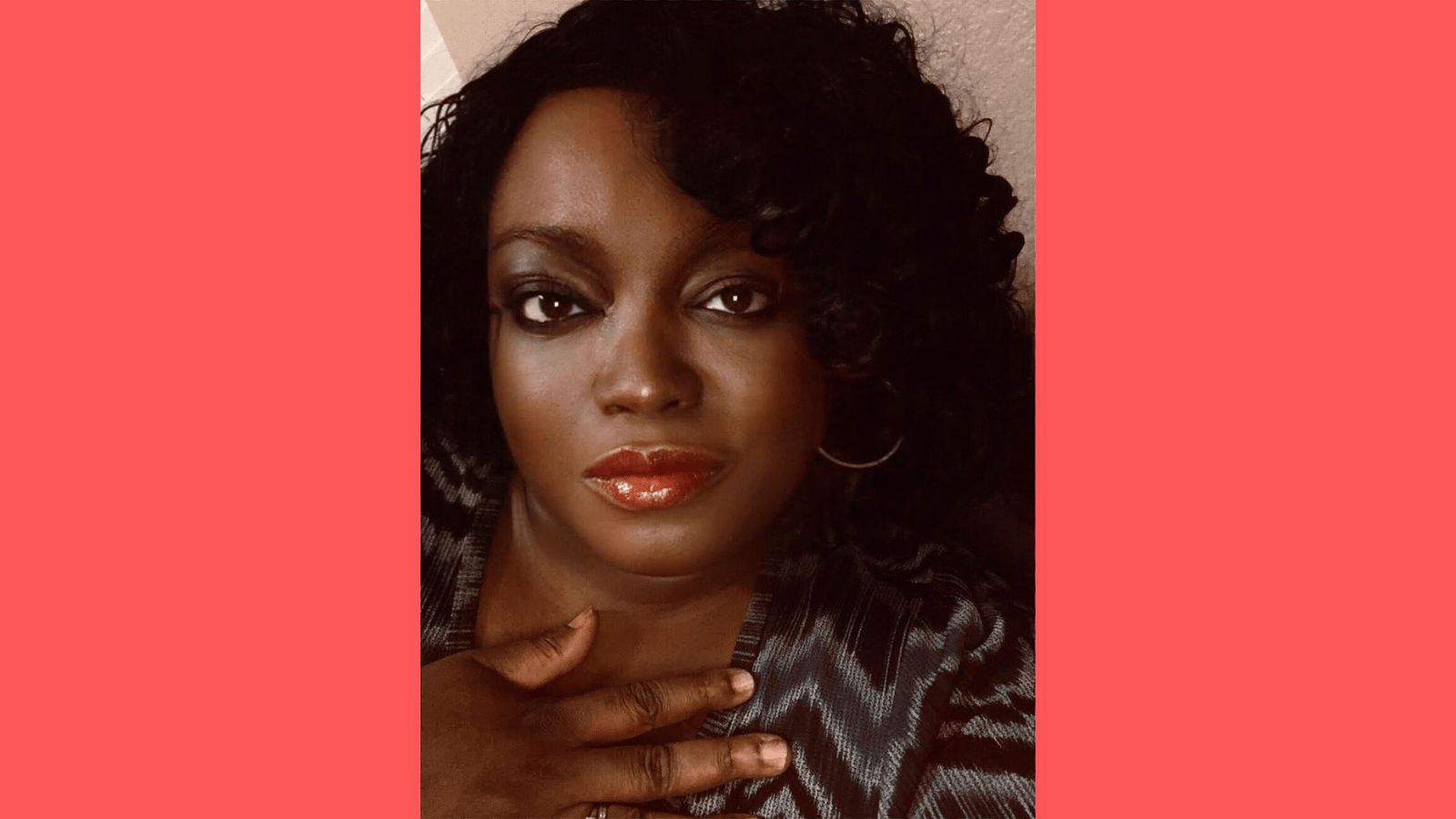 Graphic with a coral background and a head and shoulders picture of Tinu Abayomi-Paul, against a light brown walk. She is a dark skinned woman with chin length curly black hair. She has on red lipstick and her left gold colored hoop earring is visible. She is not smiling, but looks content. She has a hand lightly pressed against her chest and is wearing a dark blue, light blue and black blouse patterned in zigzag stripes. She's looking directly into the camera.