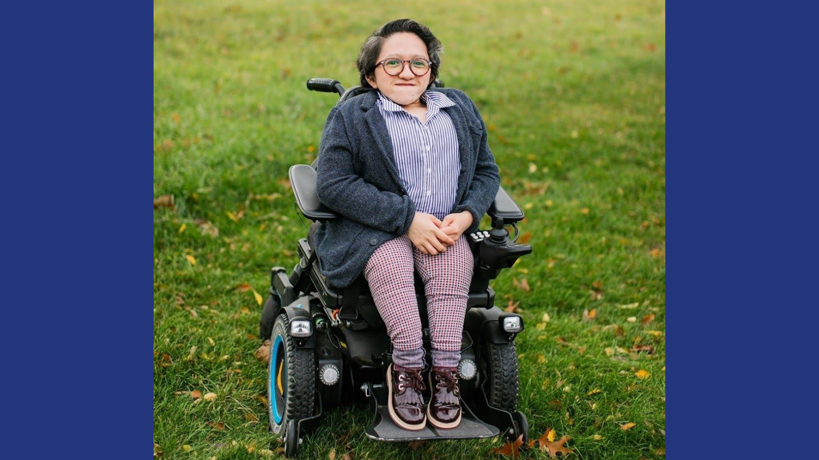 Graphic with a navy blue background featuring a photo of Sandy Ho sitting in her power wheelchair in the middle of a field of green grass, with houses blurred in the background. She has short dark wavy hair and tortoise shell glasses on. Sandy is wearing maroon shoes, plaid pants, a dark gray cardigan, and a button-up blue and white striped collar shirt. She is smiling at the camera with her hands in her lap.