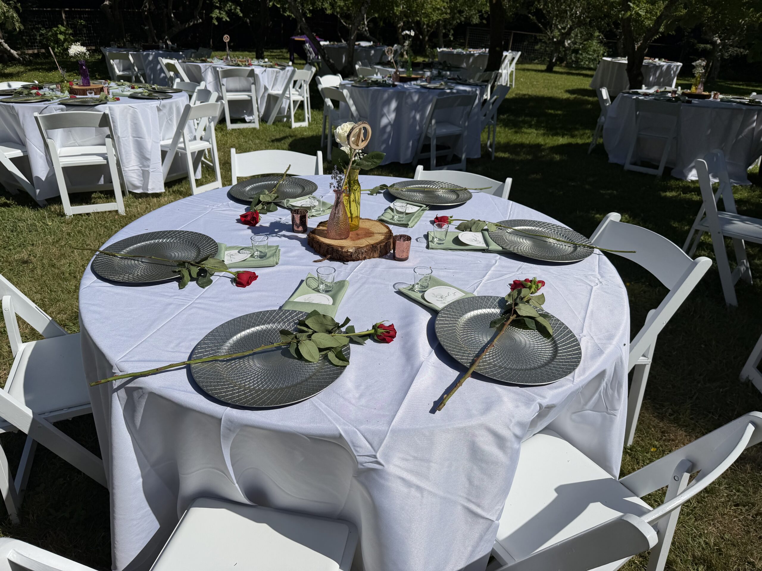 Round wedding reception table set with plates, folded napkins and simple greenery over a visibly wrinkled tablecloth.
