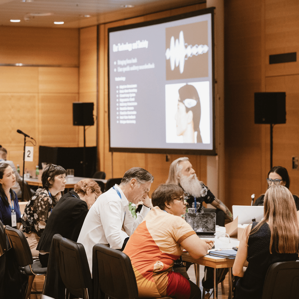 A workshop group engaged in a presentation about technology and society, with a slide showing a wearable neurotech device.