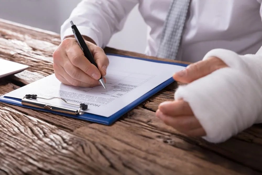 Person with a bandaged hand filling out an insurance claim form on a clipboard after a dog bite injury