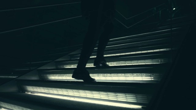 Persona subiendo escaleras en la oscuridad, representa avance constante en el camino hacia la libertad financiera.