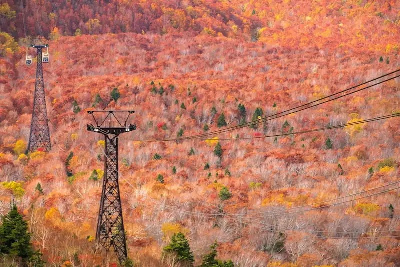 The Hakkoda Ropeway rises above Aomori Prefecture's Hakkoda mountains as the volcanic slopes turn red, orange, and gold during the autumn foliage season.