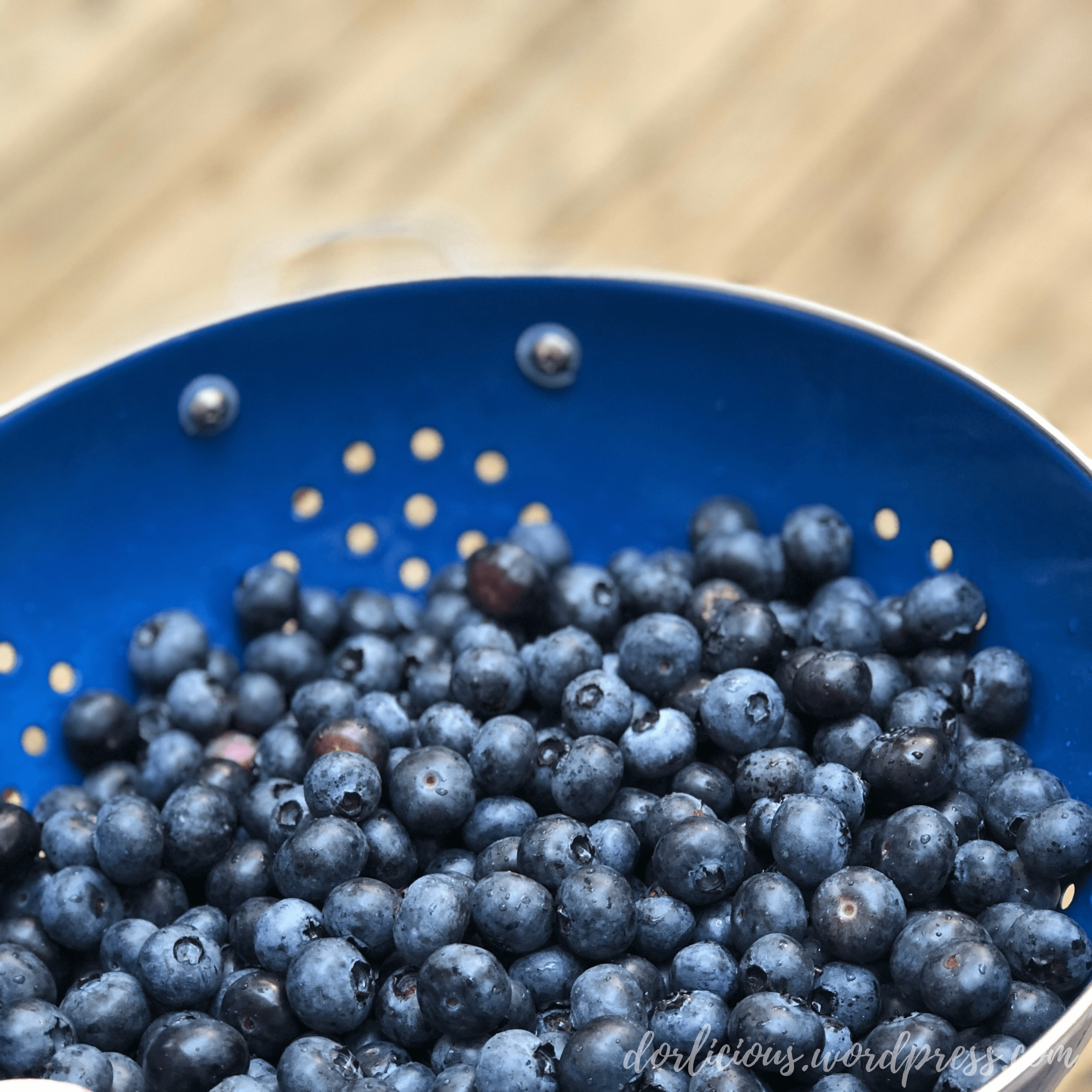 Freshly washed blueberries in a blue strainer in front of a blurred wooden background