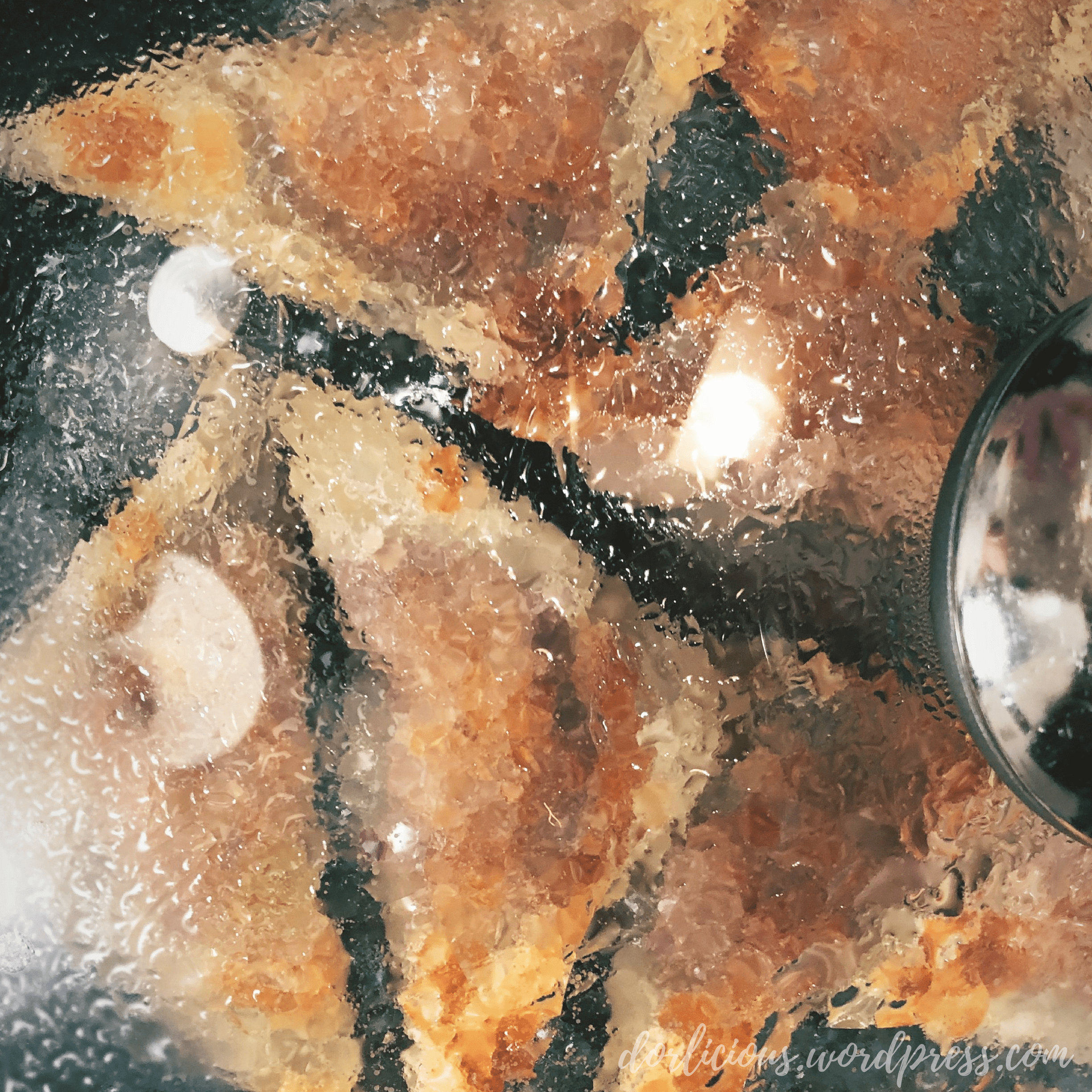Potstickers inside a pan with a glass lid placed over the top of the pan that has collected with steam