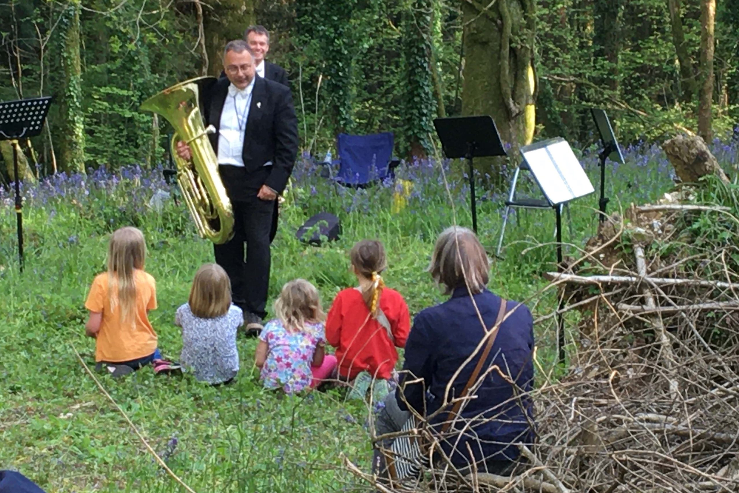 Children watch an adult musician in a woodland setting