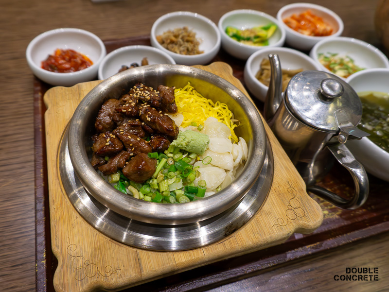 돌솥에 정갈하게 담긴 소불고기와 고명이 올라간 돌솥밥과 반찬이 보인다.